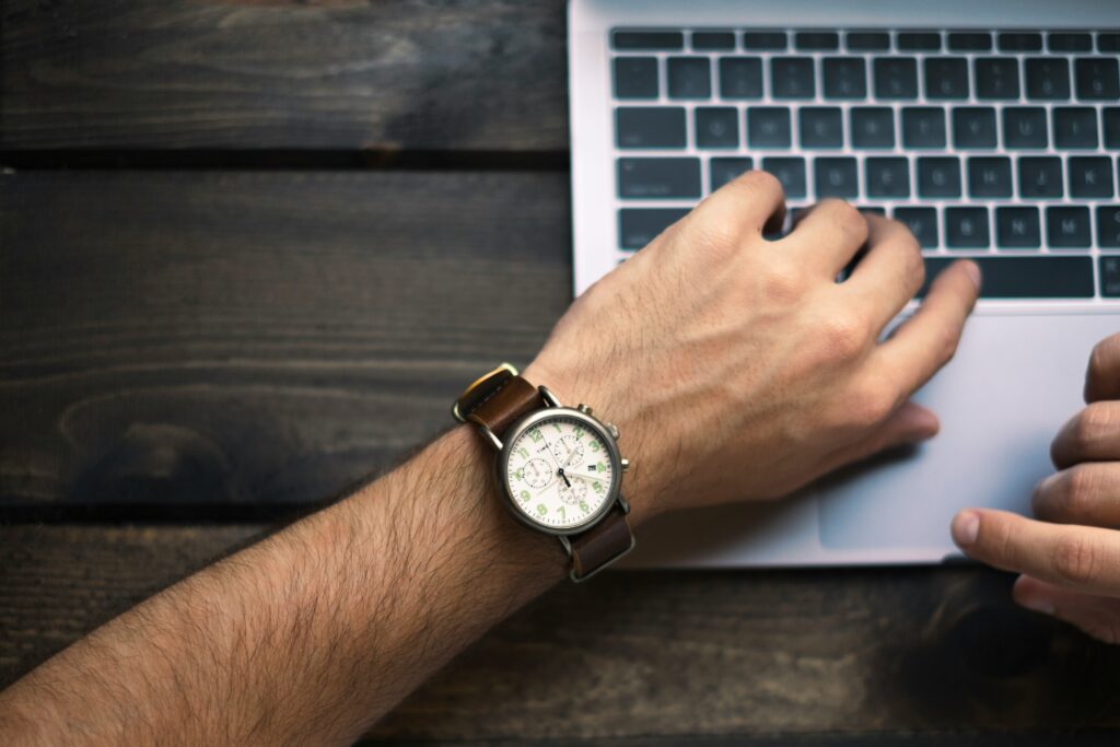 Man checking a wristwatch while working on a laptop. Pure Professional helps you manage your time effectively.